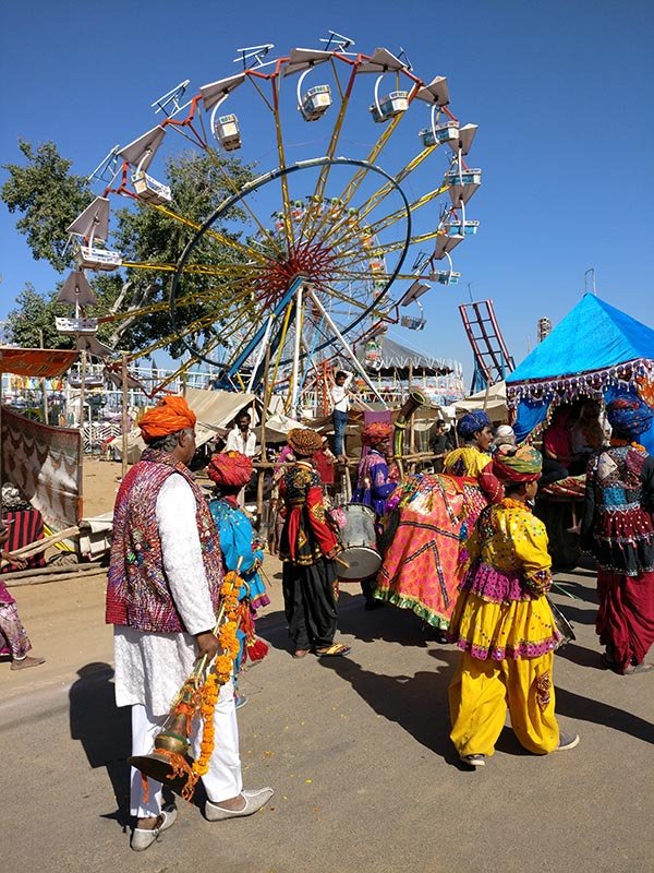 Rajasthani folk artists performing near a Ferris wheel at Pushkar Fair